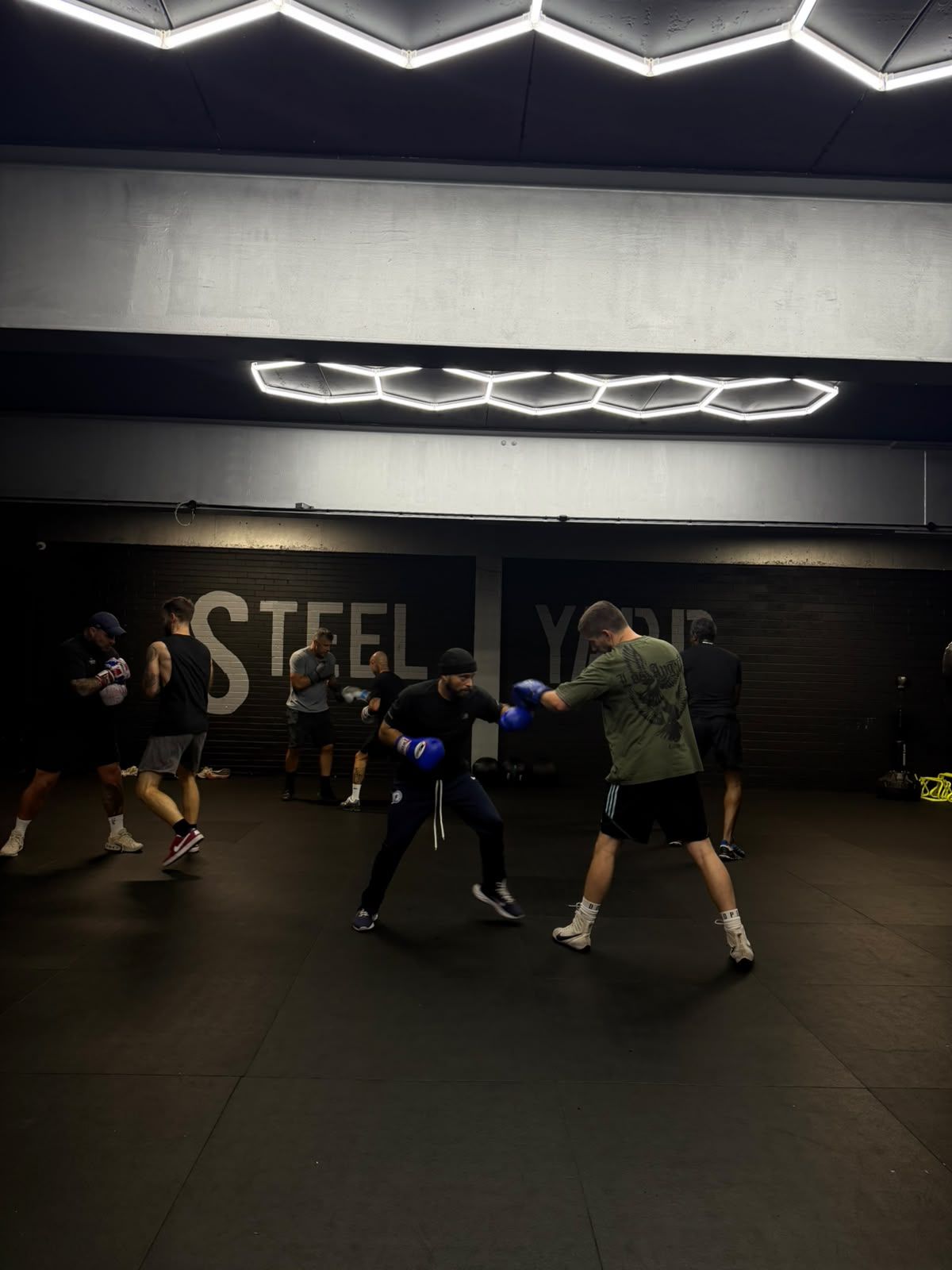 Members practising boxing pads and sparring in front of the Steel Yard wall.